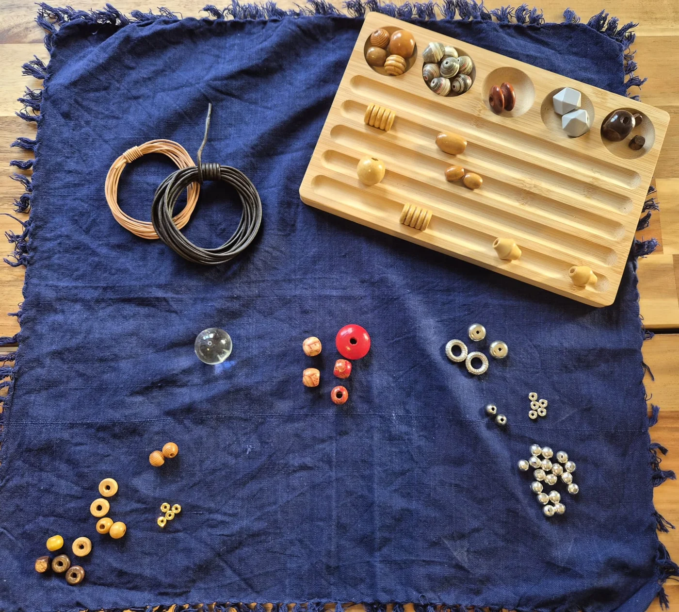 Beads, findings and cord laid out on indigo linen with a wooden bead board
